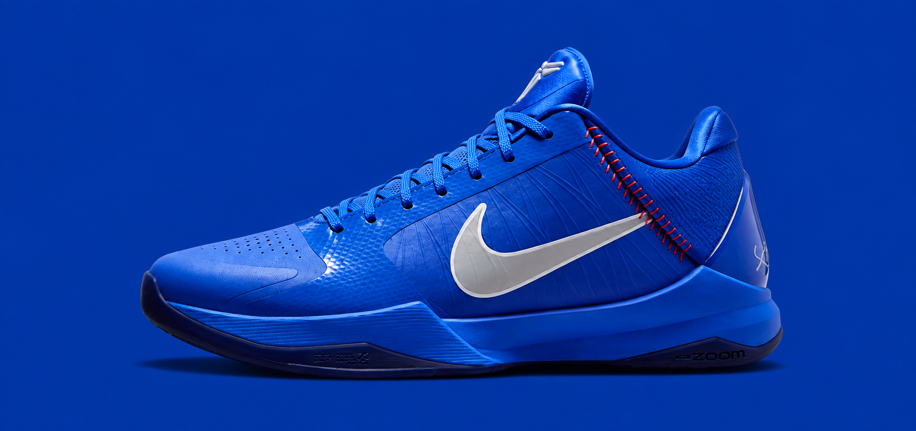 A Nike basketball shoe in a vibrant royal blue colorway, featuring a metallic silver Swoosh and subtle red stitching details, set against a solid blue background.